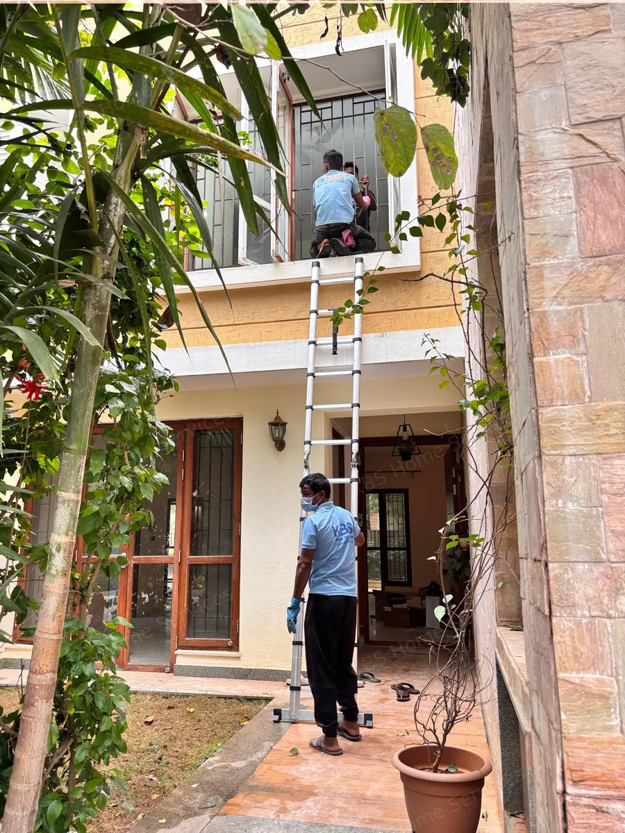 KBS team cleaning first floor balcony windows with a ladder at a Bengaluru home