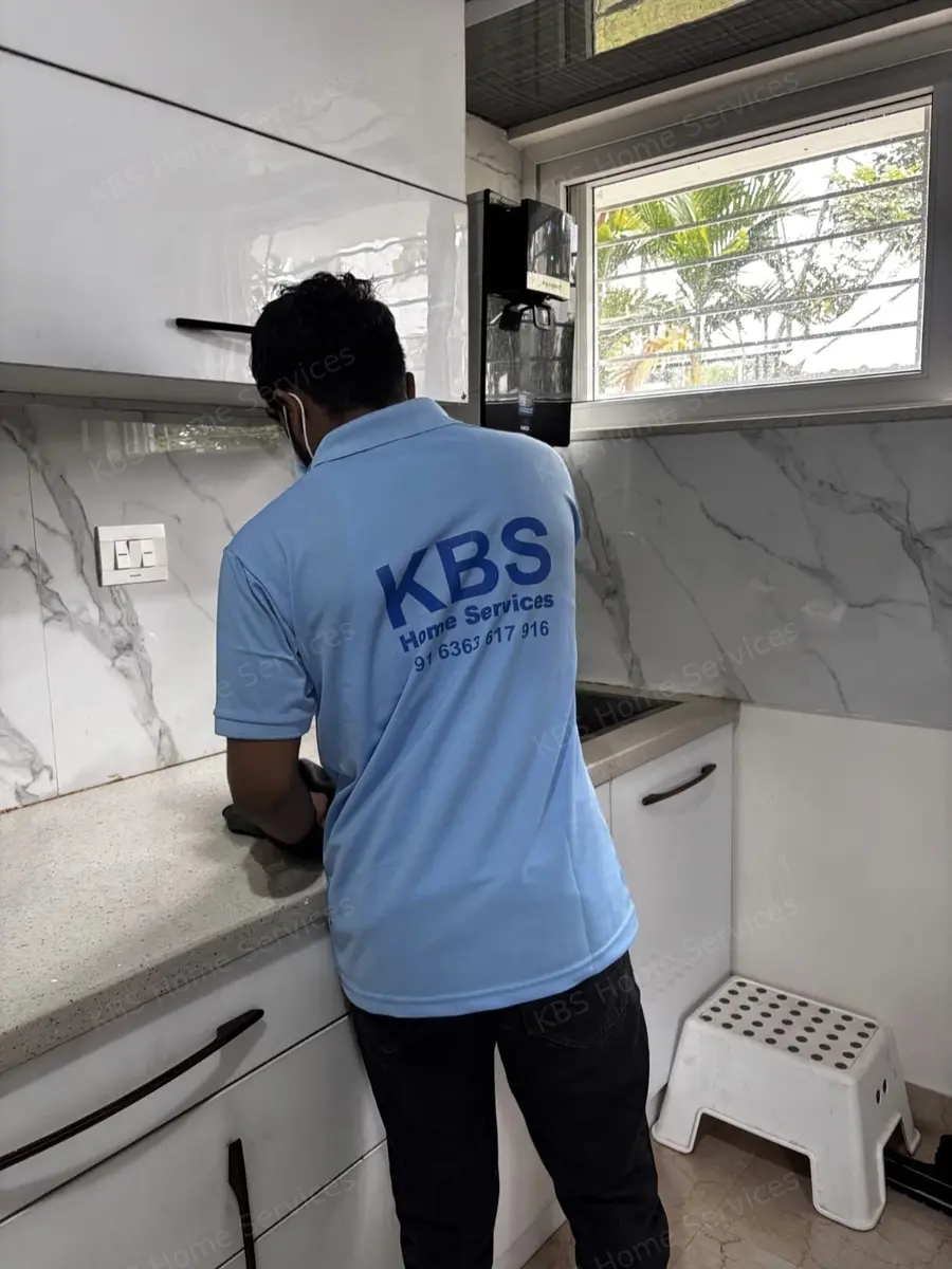 KBS technician cleaning the kitchen counter and chimney area in a Bengaluru home