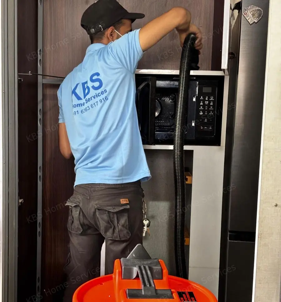 KBS technician vacuum cleaning the microwave shelf during kitchen deep cleaning